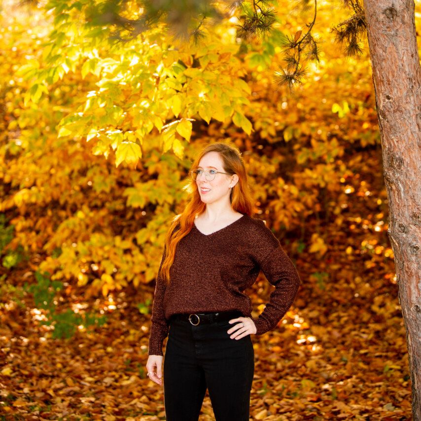 a young woman standing in front of autumn foliage looking to the left